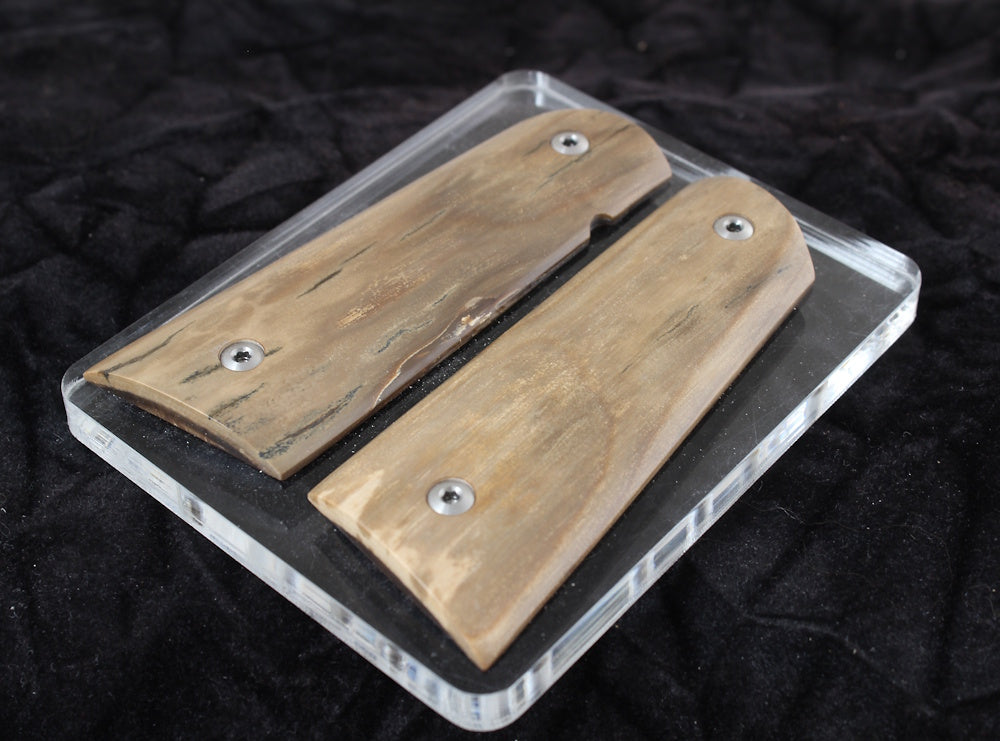 Gun grip with metal screws on a clear plastic base against a dark background