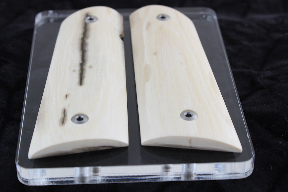 Two wooden gun grips on a clear acrylic stand against a dark background