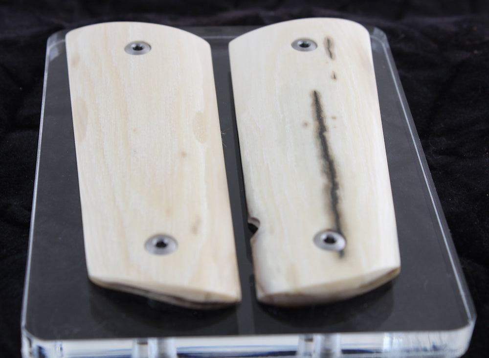 Two wooden textured ivory gun grips on a clear stand with a black background